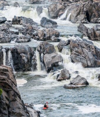 Kayaker approaches turbulent rapids among jagged rocks and small cascades