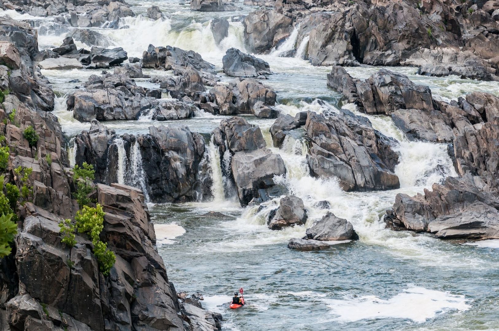 Kayaker approaches turbulent rapids among jagged rocks and small cascades