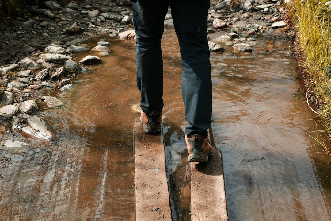 Hiker crossing a shallow rocky stream on wet wooden planks